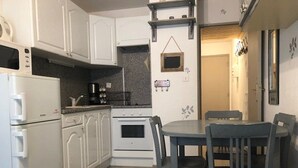Cozinha compacta com armários brancos, fogão, micro-ondas e uma mesa de jantar com cadeiras.