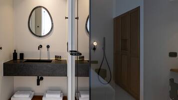 Un baño moderno con separador de vidrio, un espejo redondo, un lavamanos oscuro y un mueble de madera.