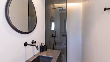 Un baño moderno con un espejo redondo, un lavamanos rectangular y una zona de ducha.