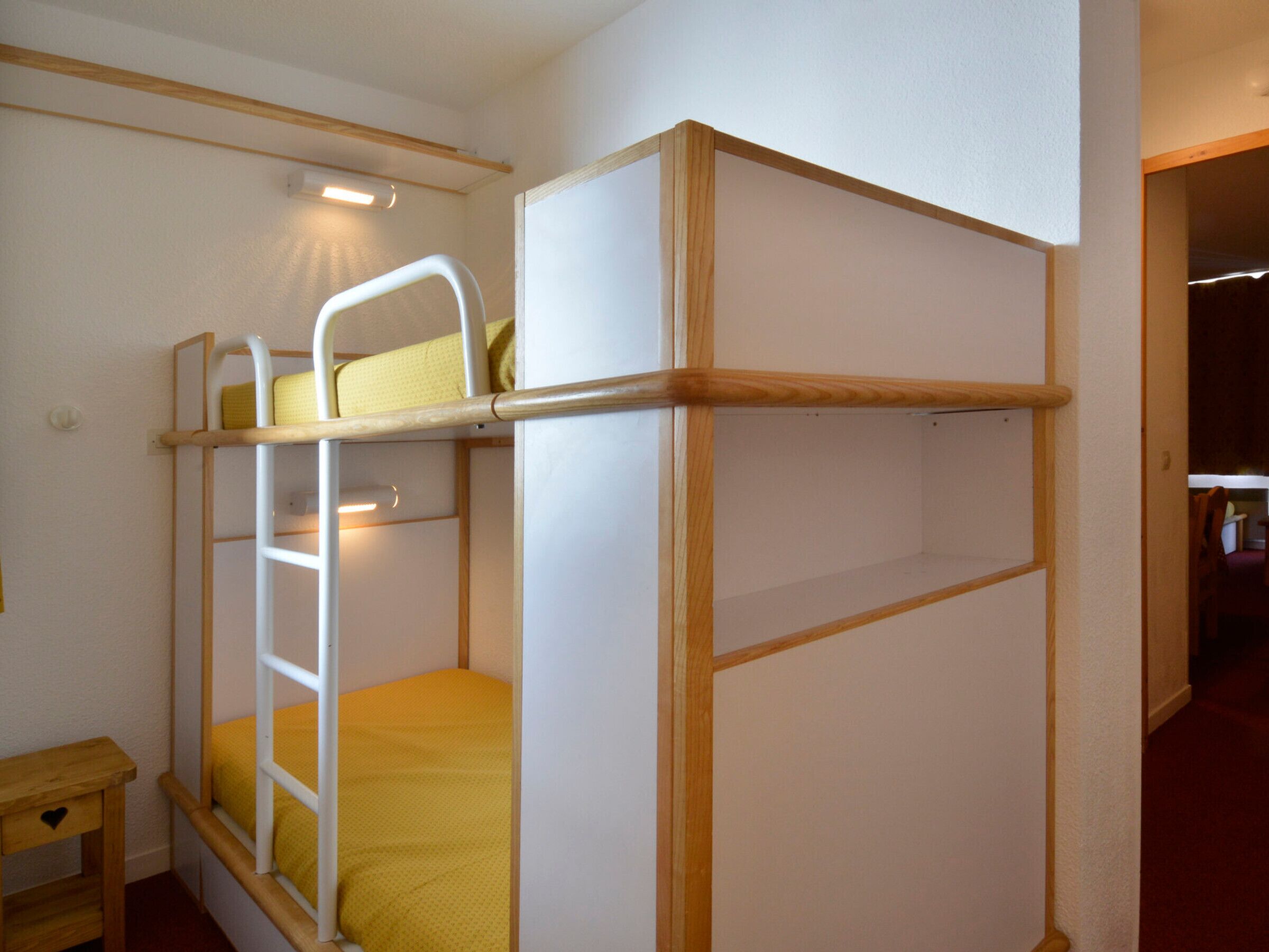 A bunk bed with a wooden frame and a yellow mattress. There is a small wooden nightstand with a drawer and a heart-shaped object on it.