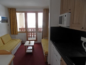 A compact room with a bed, a small table, a microwave, and a kitchenette.