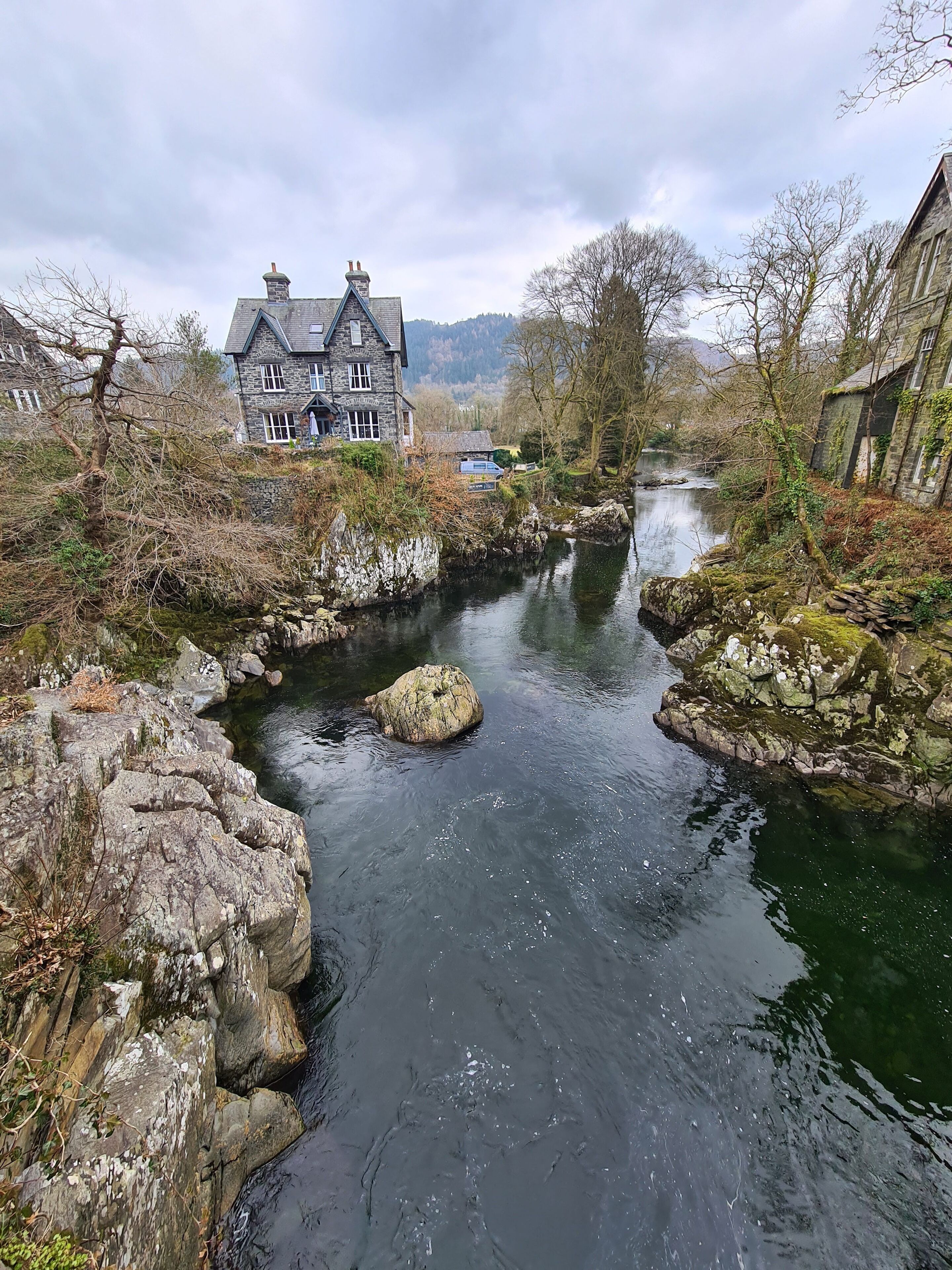 Un edificio de piedra con diseño tradicional, un río con rocas y vistas del paisaje circundante.