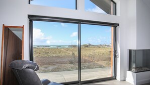 Ein modernes Zimmer mit einer großen Schiebeglasdoor zum Meerblick, ein bequemer Ledersessel und ein eingebauter Kamin.