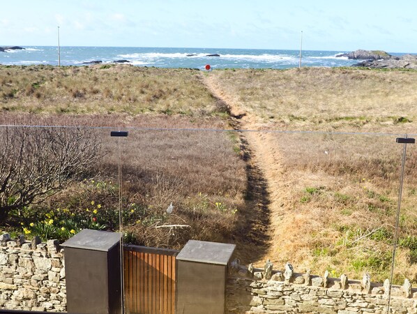 Un sendero costero que lleva al mar, bordeado por muros de piedra y una valla de madera.