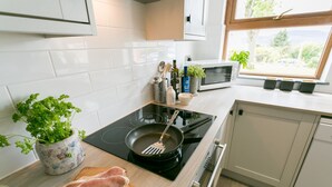 A modern kitchen with white cabinets, a black induction cooktop, a wooden cutting board with raw meat, a frying pan, and a potted plant.