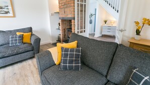 A living room with a grey sofa set, a brick fireplace, and a staircase leading to another room.