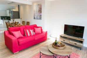 A modern living room with a red sofa, a wooden coffee table, and a TV on a wooden stand.