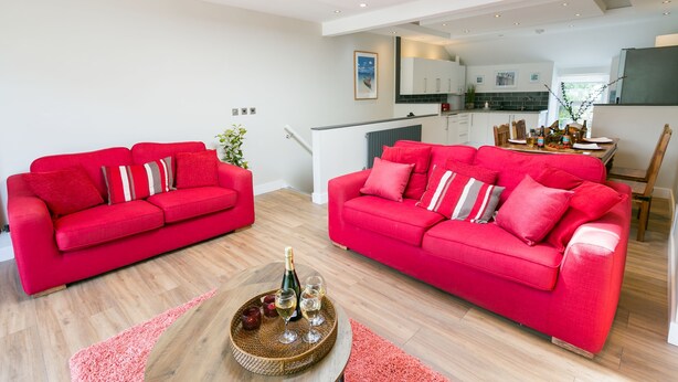 A modern living room with two red sofas, a wooden coffee table with drinks, and a kitchen in the background. - 10 Beach Road -  a sea view that sleeps 4 guests  in 2 bedrooms (Menai Bridge)