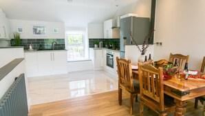 A modern kitchen with white cabinets, a wooden dining table, and a view of the outdoors. - 10 Beach Road -  a sea view that sleeps 4 guests  in 2 bedrooms (Menai Bridge)
