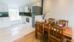 A modern kitchen with white cabinets, a stainless steel refrigerator, and a dining table set with chairs. - 10 Beach Road -  a sea view that sleeps 4 guests  in 2 bedrooms (Menai Bridge)