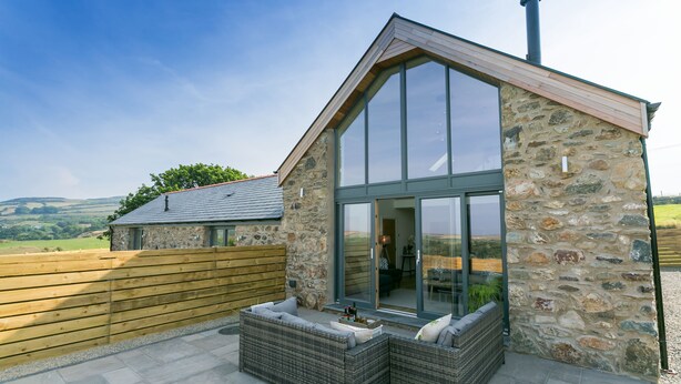 A stone building with large windows and a wooden deck. - Bwncath -  a coastal that sleeps 6 guests  in 3 bedrooms (Llanfairynghornwy)