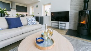 A modern living room with a sofa, a coffee table with a tray of snacks and drinks, a fireplace, and a TV. - Bwncath -  a coastal that sleeps 6 guests  in 3 bedrooms (Llanfairynghornwy)