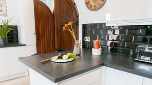 Uma cozinha com bancada de mármore, porta de madeira, relógio e painel de azulejos pretos.