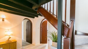 Uma escada com corrimãos de madeira que leva a um andar superior, uma mesa de consola de madeira com uma luminária e um vaso de planta.