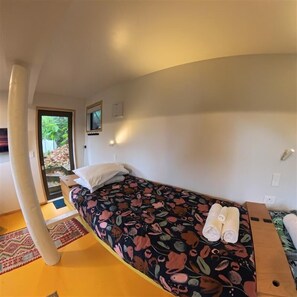 A single bed with a floral bedspread, a wooden nightstand, and a small table with a towel. - Kundaniwas - Lake Okareka Tiny House, Kayaks (Rotorua)