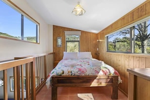 Un dormitorio con cama de madera, ventanas amplias y un balcón.