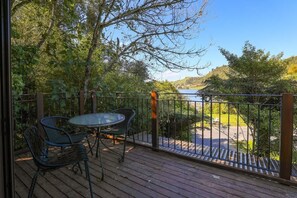 A wooden deck with a metal railing, a glass table, and two chairs. - Kundaniwas - Lake Okareka Tiny House, Kayaks (Rotorua)