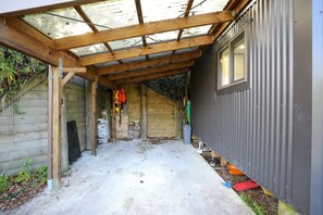 A covered outdoor area with a wooden structure, a concrete floor, and a corrugated metal wall. - Kundaniwas - Lake Okareka Tiny House, Kayaks (Rotorua)