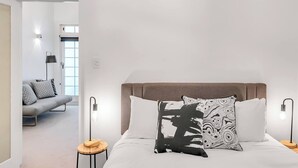 A modern bedroom with a bed, two bedside lamps, and a sofa in the adjacent room. - 'Latitude' - Stunning Opera House Views, Designer 2 Bedroom Executive Apartment w/ airconditioning (Kirribilli)