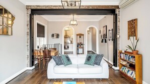 A spacious living room with a white sofa, two patterned cushions, a coffee table, and a bookshelf filled with books. - 'Latitude' - Stunning Opera House Views, Designer 2 Bedroom Executive Apartment w/ airconditioning (Kirribilli)