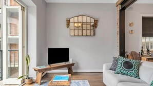 A living room with a flat-screen TV on a wooden stand, a white sofa with patterned cushions, a potted plant, and a rustic chest of drawers. - 'Latitude' - Stunning Opera House Views, Designer 2 Bedroom Executive Apartment w/ airconditioning (Kirribilli)