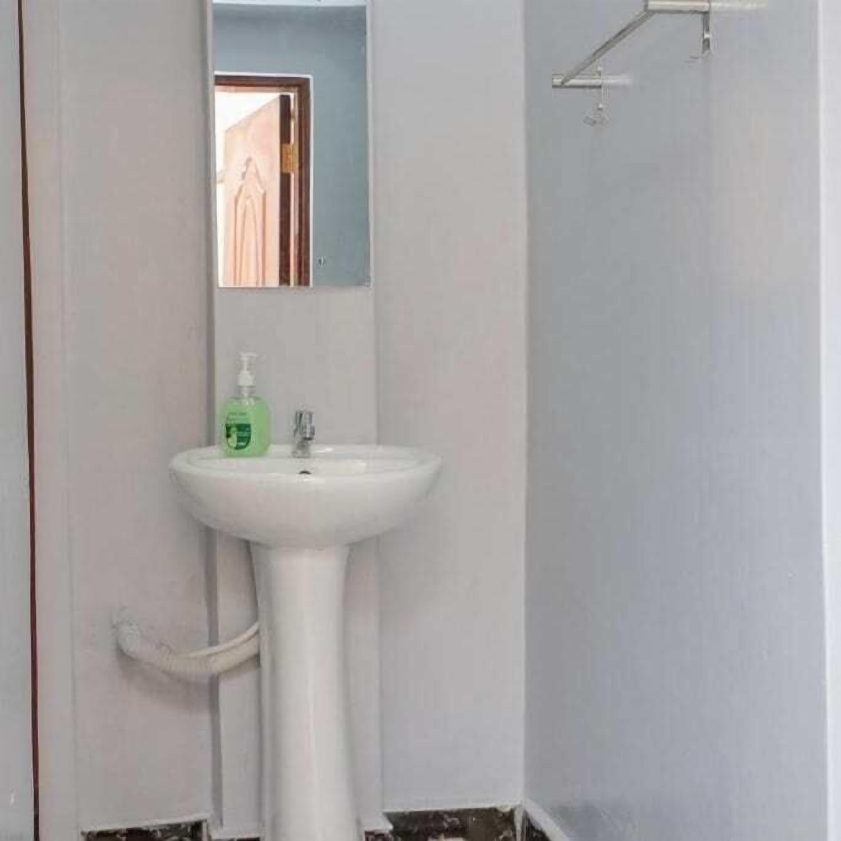 A bathroom with a pedestal sink, a mirror above it, and a shower area to the right.