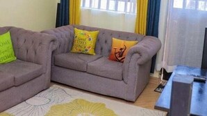 A living room with a grey sofa, yellow and blue curtains, and a window with a grid pattern.