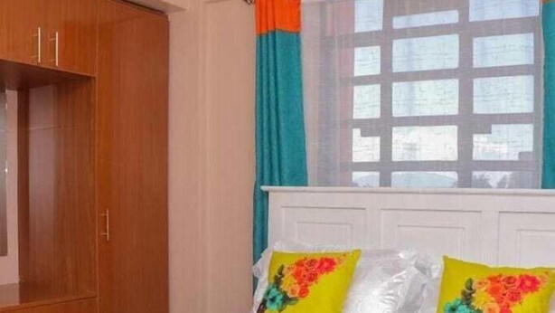 A bedroom with a bed, wooden wardrobe, and curtains.