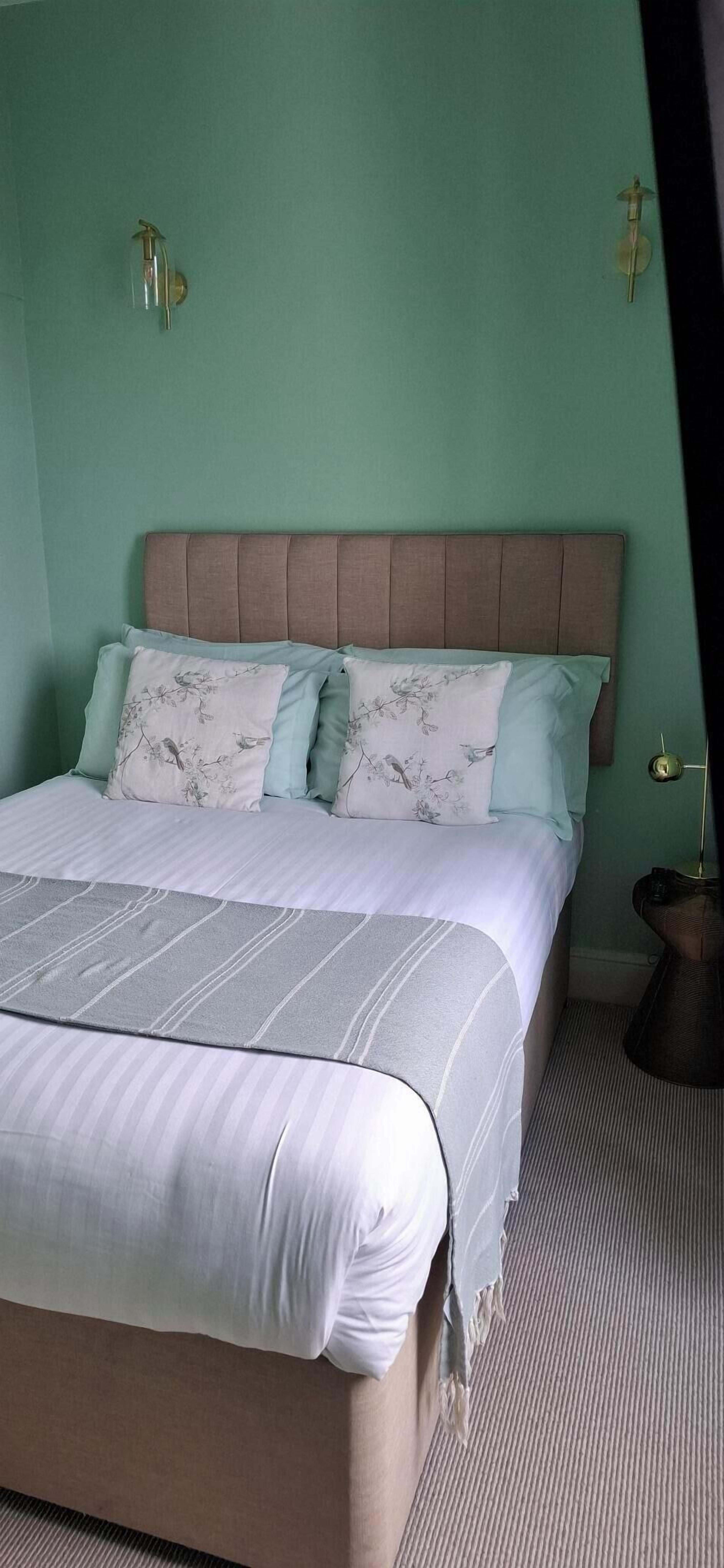A neatly made bed with a striped bedspread, a padded headboard, and floral-patterned pillows.