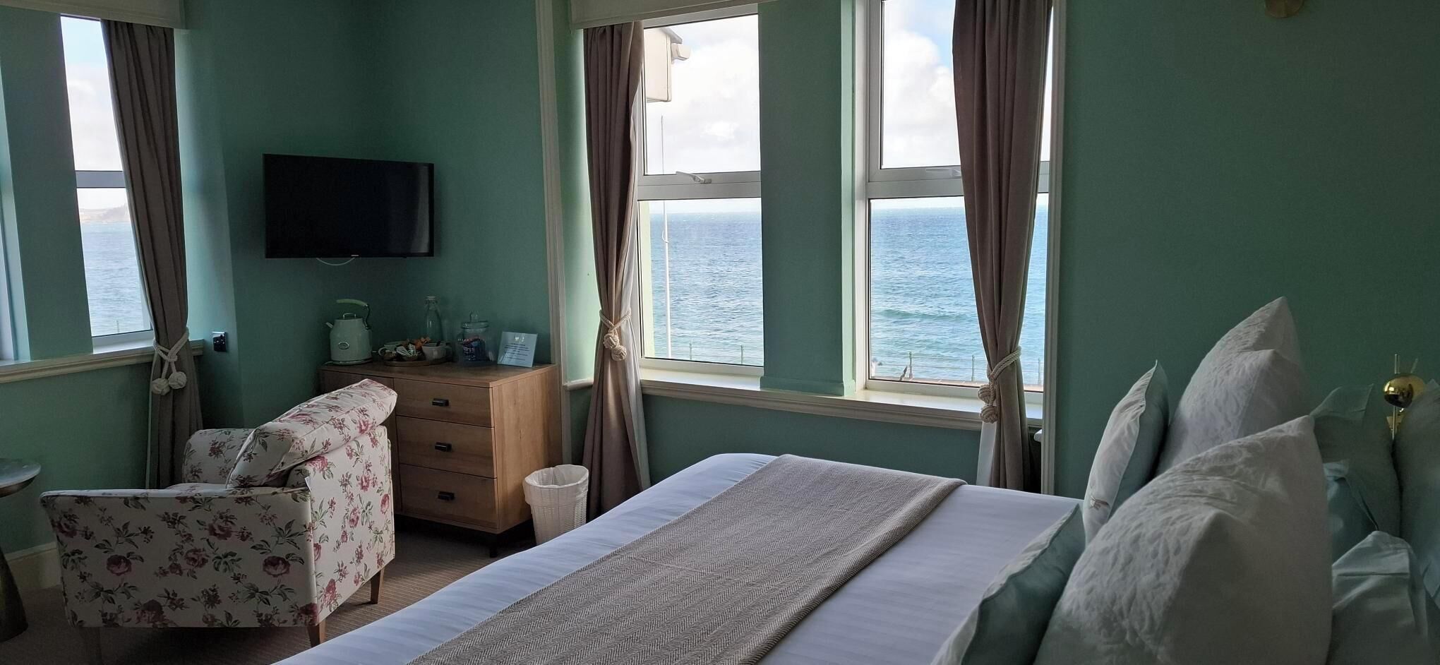 Een slaapkamer met een bed, een dressoir, een stoel, een televisie en uitzicht op zee.
