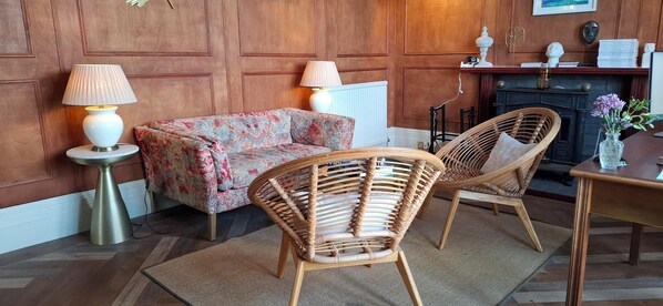 A room with wooden paneled walls, a patterned sofa, two wicker chairs, a small table, and two lamps.