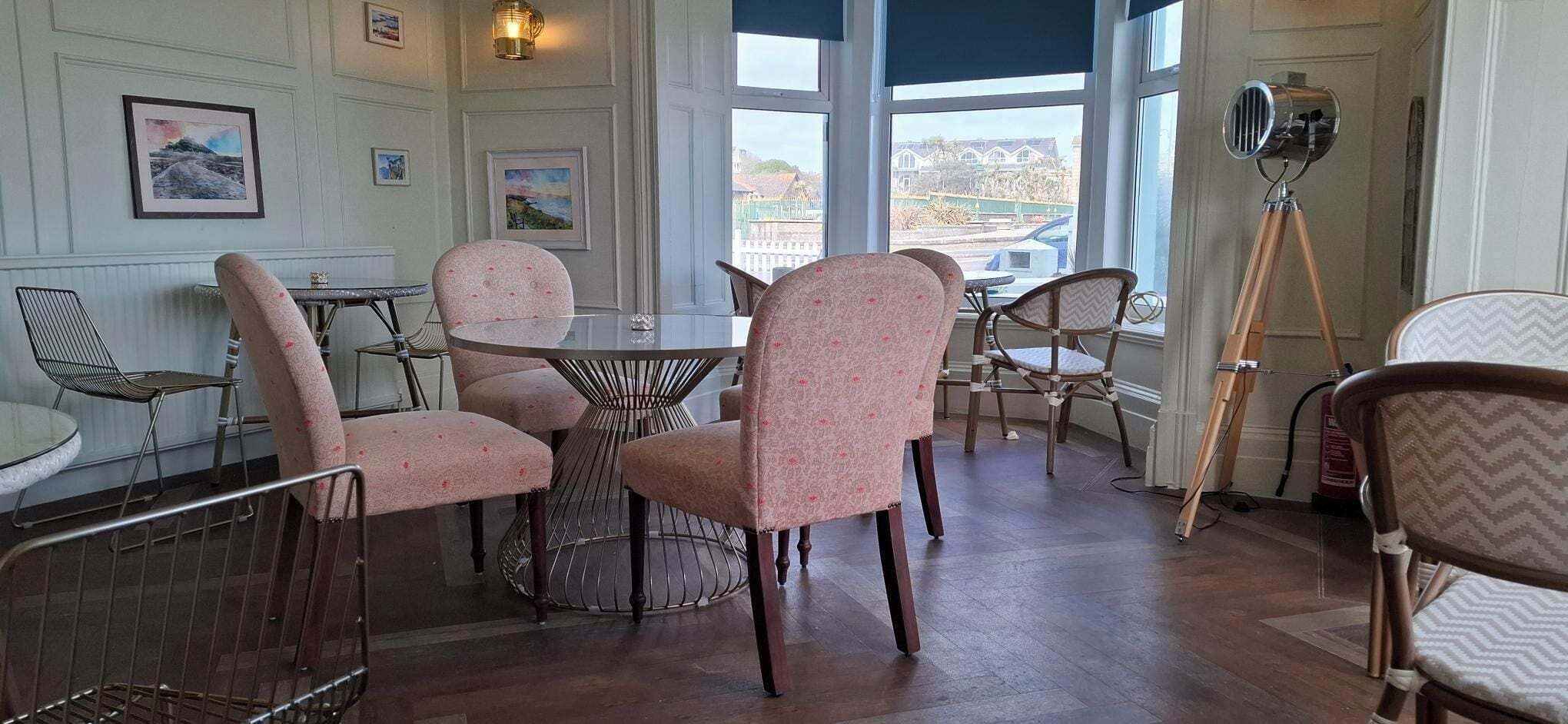 Een eetgedeelte met ronde tafels en gestreepte stoelen, grote ramen met uitzicht en een op een statief gemonteerde camera.
