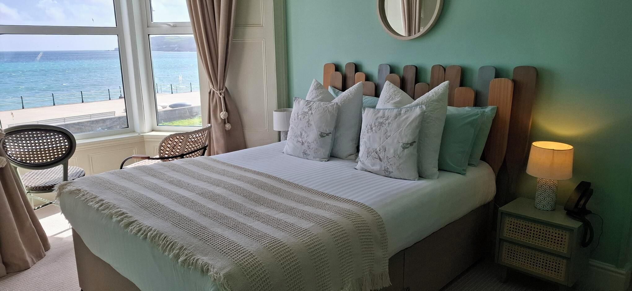 Un lit avec une couverture à rayures, une lampe de chevet et une vue sur la mer par la fenêtre.