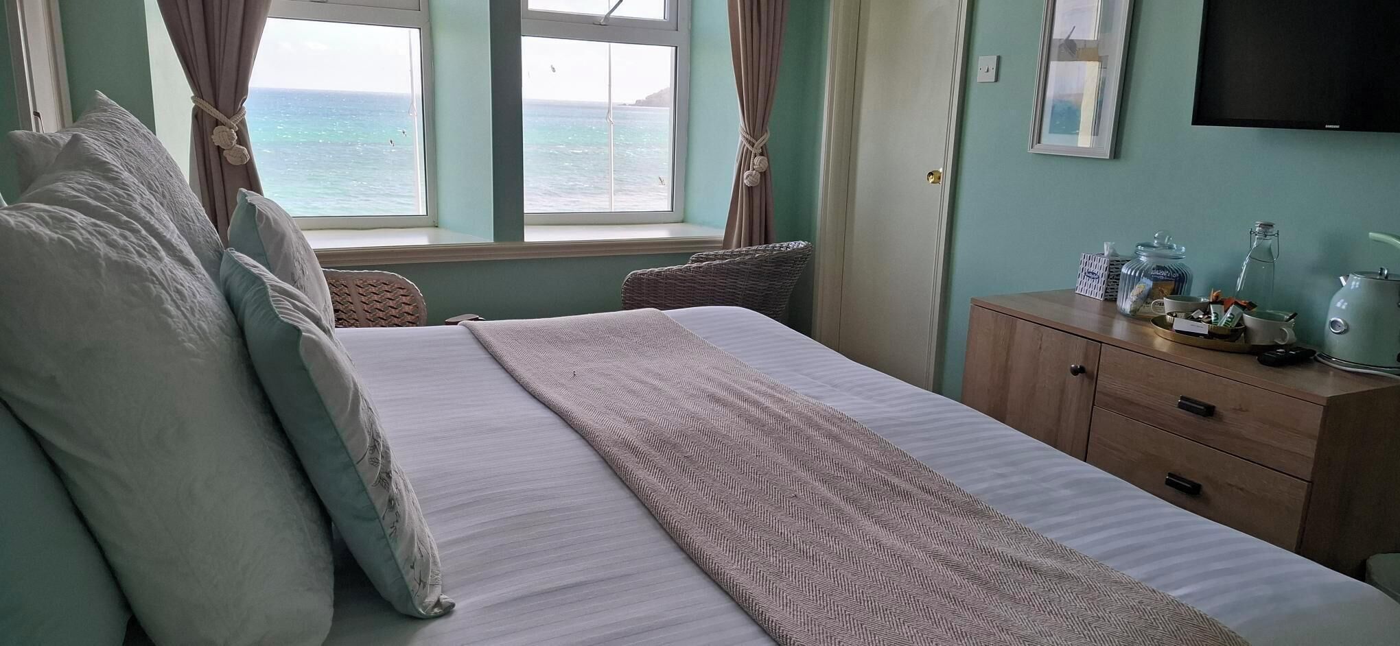 Une chambre à coucher avec un lit, une fenêtre avec des rideaux, une commode avec des articles de toilette et un téléviseur fixé au mur.