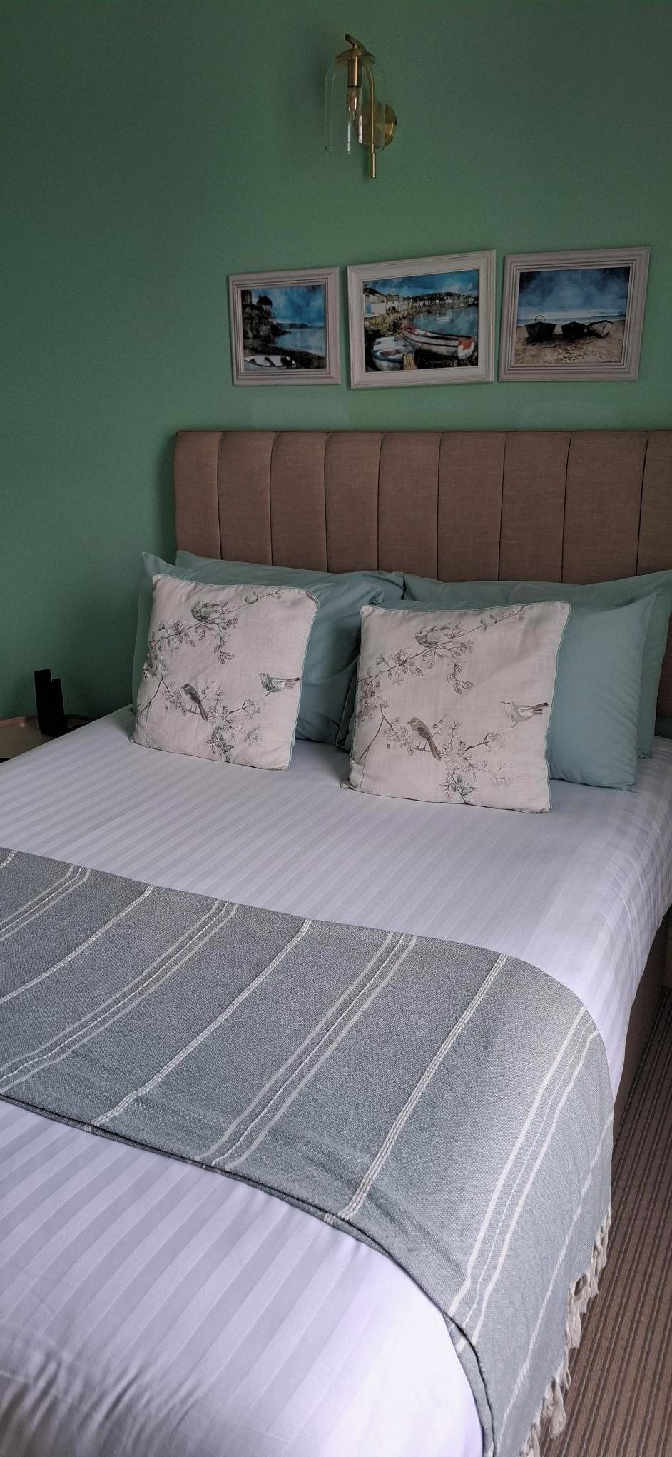 A bed with a striped blanket, two pillows with bird patterns, a headboard, and three framed pictures on the wall.
