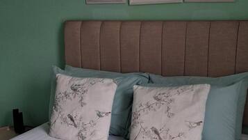 A bed with a striped blanket, two pillows with bird patterns, a headboard, and three framed pictures on the wall.