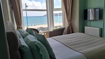 Habitación de hotel con cama, una silla, televisión y vista al mar.