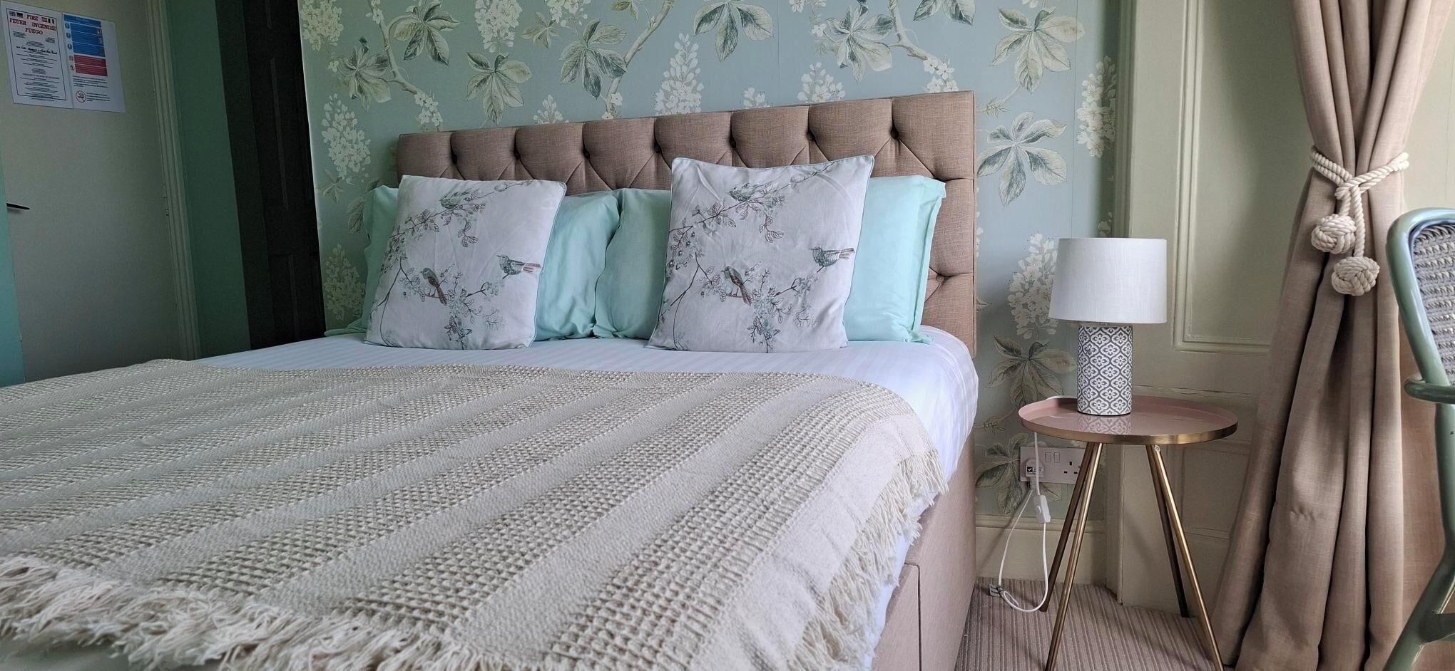 A bed with a tufted headboard, multiple pillows, a bedside lamp, and a small round table with a lamp.