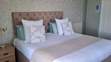 A neatly made bed with a patterned headboard, a bedside lamp, and a drawer unit.