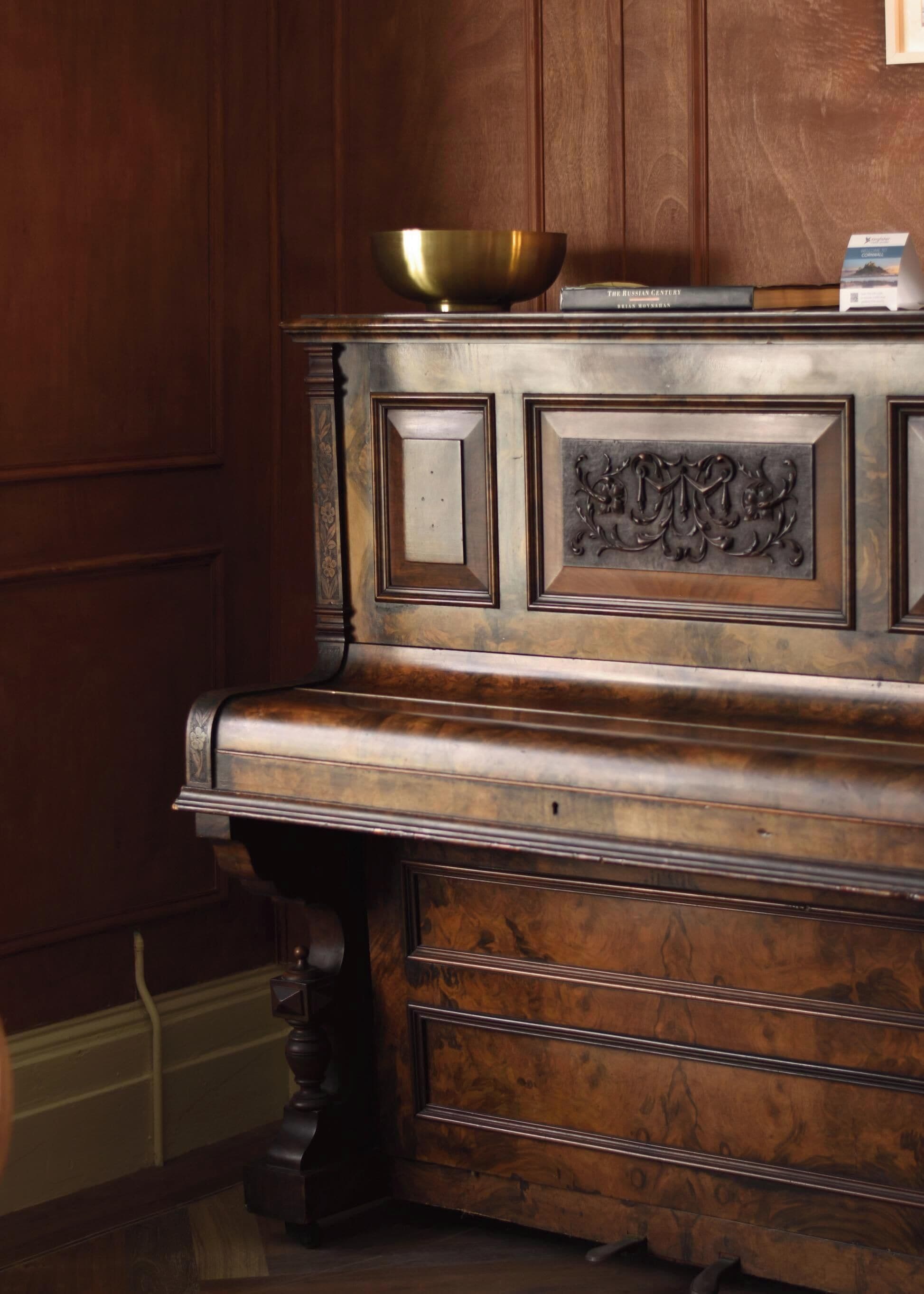 A wooden piano with a brass bowl on top, a book titled 'The Russian Century,' and a small brochure on the right.