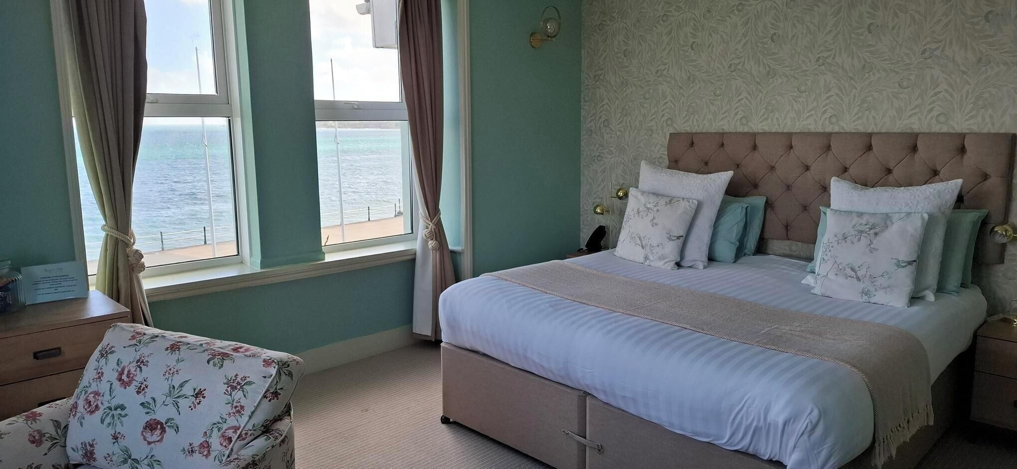 Un dormitorio con cama, cortinas, una silla y vista al mar.