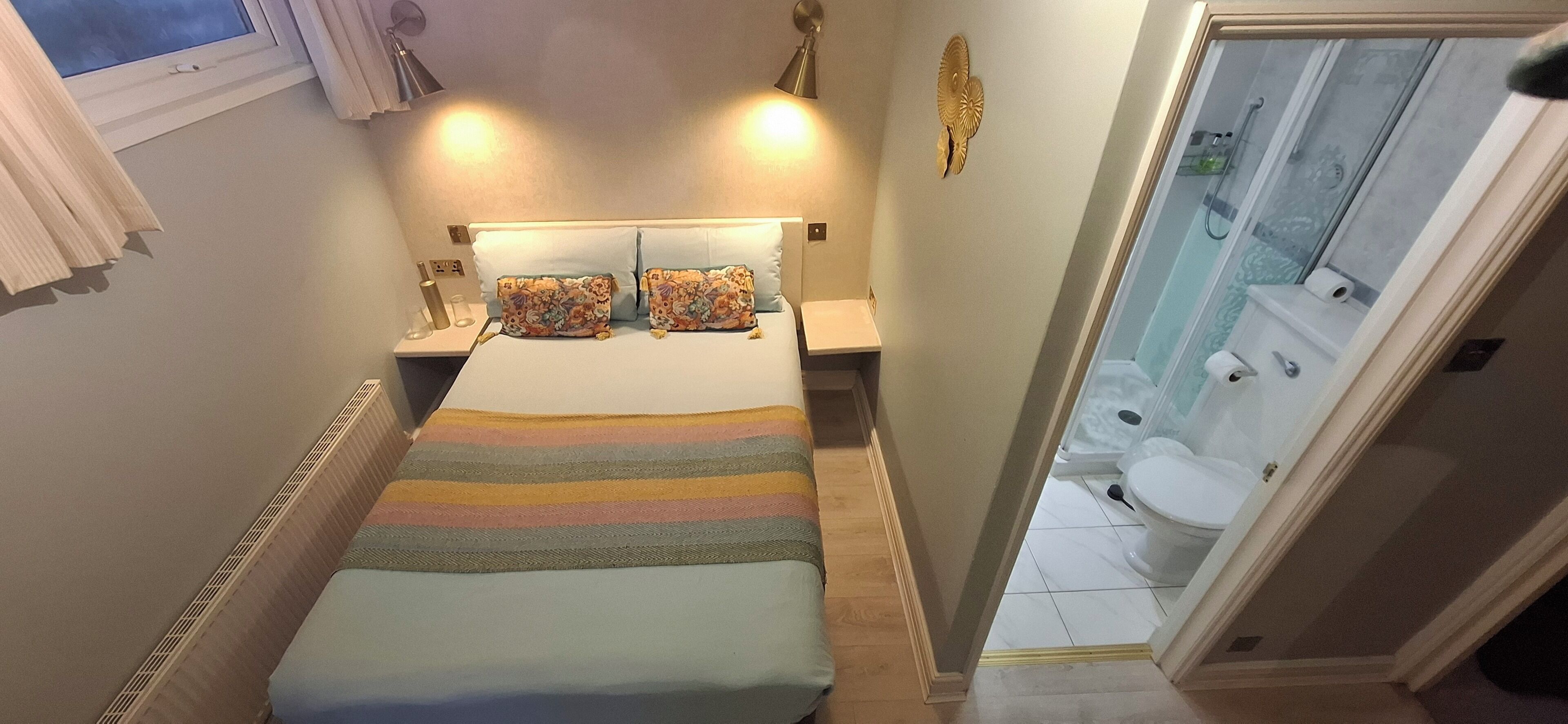 A bedroom with a bed, two bedside tables, a nightstand, a window with curtains, and a view of a bathroom.