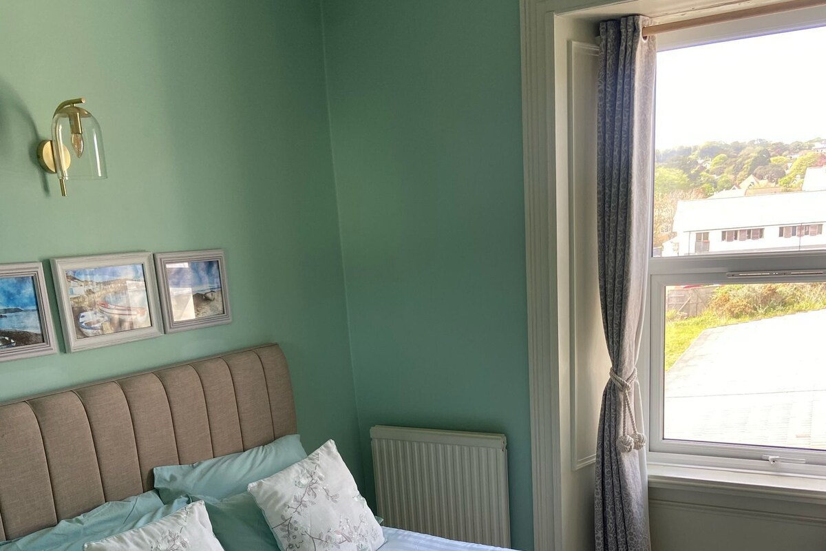 A bedroom with a bed, a radiator, a window with curtains, and three framed pictures on the wall.