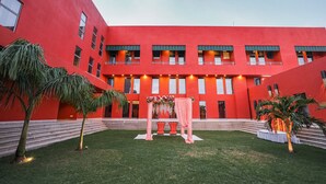 Un bâtiment rouge doté d’une cour, de palmiers et d’une arche décorée.