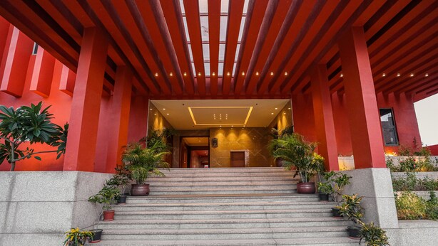 L’entrée d’un immeuble se distingue par sa façade rouge, un escalier en pierre et des plantes en pot.