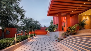 Un chemin pavé mène à un bâtiment aux murs rouges et oranges, entouré de verdure et de plantes en pot.