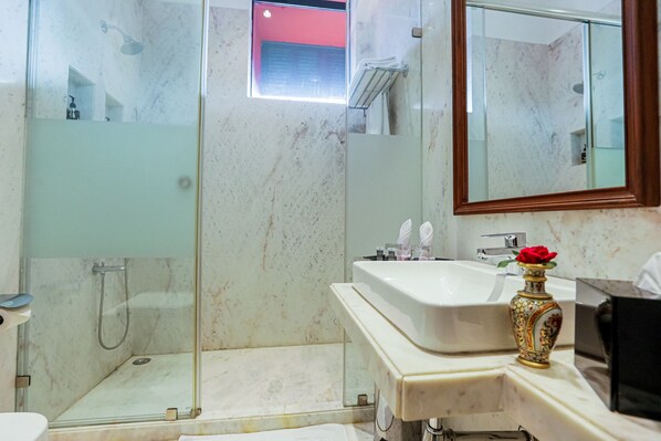 A bathroom with a glass-enclosed shower, a sink with a vase of a red rose, and a mirror.