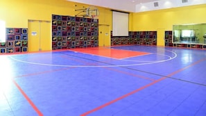 Un gimnasio con piso azul, aro de baloncesto y decoraciones coloridas en las paredes.