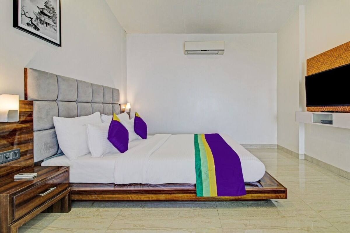 A modern hotel room with a large bed, a TV mounted on the wall, and a wooden nightstand.