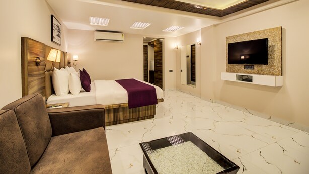 Una habitación de hotel con cama, televisor montado en la pared, una zona de estar y una mesita con un objeto decorativo.